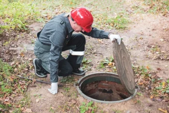 A septic worker in a hard hat lifts a manhole cover on a septic lift station.