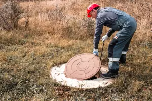 A septic worker in a hard hat lifts a manhole cover of a lift station.